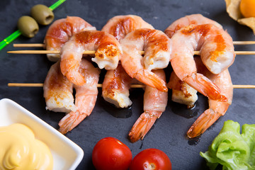 Shrimps grill in prosciutto with sauce on a black board. Close-up, selective focus.