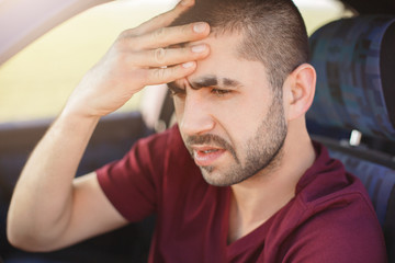 Fatigue male driver keeps hand on forehead, has headache after being long time in car, dressed casually, thinks about future trip. Professional man drives automobile. People and transport concept