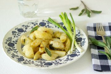 Young fried potatoes with onions and sage in a light plate on a light table.