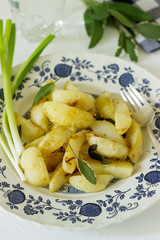 Young fried potatoes with onions and sage in a light plate on a light table.