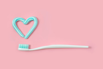 Toothbrushes and turquoise color toothpaste in shape of heart on pink background. Dental and...