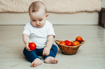 little baby girl sitting on the floor and playing with tomatoes