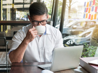 Businessman drinking coffee or tea while using laptop computer in a coffee shop