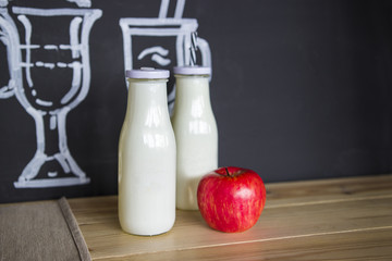 Two glass white bottles and a fresh apple on the table.