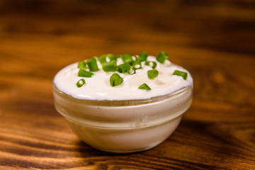 Glass bowl with sour cream and chopped green onion on wooden table