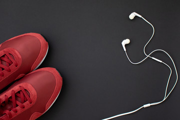Fitness flat lay. Healthy lifestyle and sport concept. Red sneakers and white earphones on a black background.