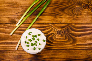 Glass bowl with sour cream and green onion on wooden table. Top view