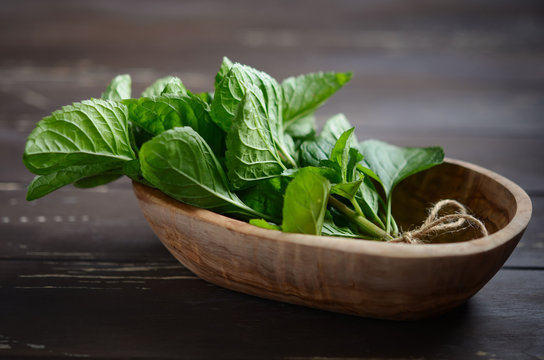 Fresh organic mint bunch in a wooden bowl on the old rustic wooden table.