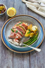 Bacon-wrapped haddock stuffed with crayfish tails, with lemony new potatoes, green beans and olives - high angle view