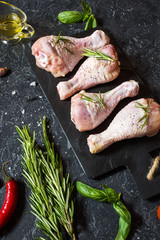 Raw uncooked chicken legs, drumsticks on stone board, meat with ingredients for cooking.