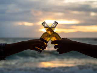 Couple hands holding beer bottles and clanging on the sunset beach. Party, Holiday, Summer,...