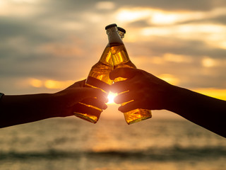 Couple hands holding beer bottles and clanging on the sunset beach. Party, Holiday, Summer,...