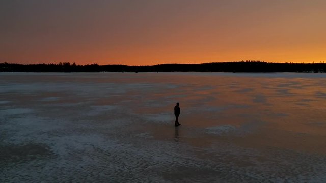 Drone shot, person walking on ice during orange sunset in the wilderness of Sweden