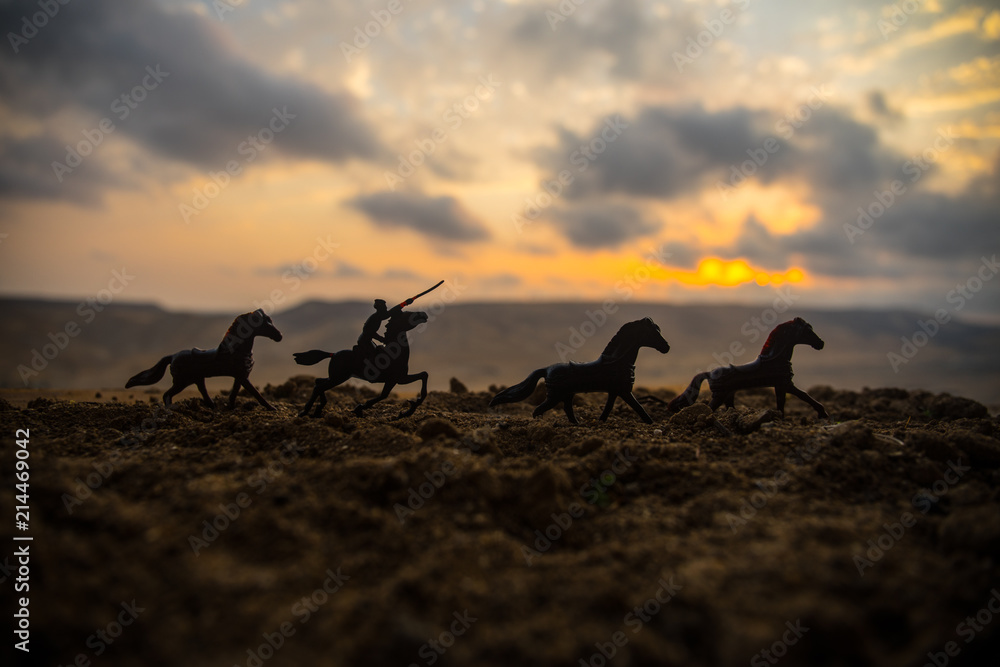 Wall mural World war officer (or warrior) rider on horse with a sword ready to fight and soldiers on a dark foggy toned background. Battle scene battlefield of fighting soldiers. Selective focus