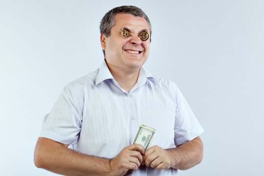 Businessman with bitcoins in his eyes smiles broadly. He holds in his hands bills of dollars