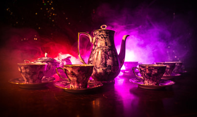 Food background tea and coffee theme. Old vintage ceramic tea or coffee pot with cups jug and sugar cup on dark background with lights and smoke. Silhouettes of ceramic tea pot and cup.
