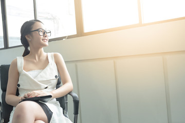 Young business woman in white dress who is candidate sitting wait for interview while looking out of big window.