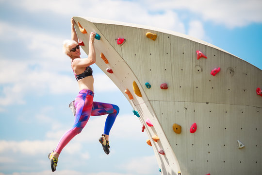 Photo from side of sports woman in leggings hanging on wall for climbing against blue sky
