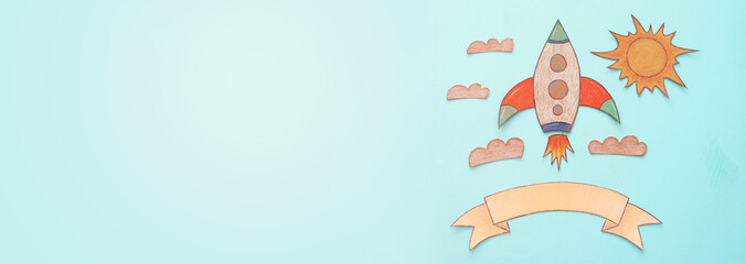 Banner of Rocket cut from paper and painted over wooden blue background.
