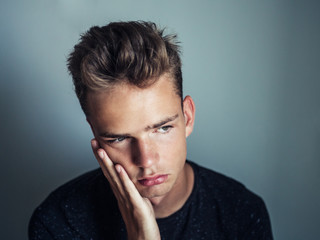 portrait of a tired sad young man,
a teenager is holding his cheek, a toothache
