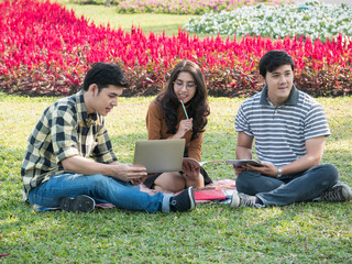 Group of college students with laptop and tablet computer while doing homework at park. Education concept.