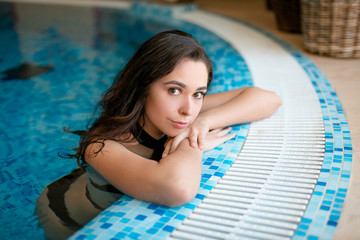 Beauty and body care. Seductive woman in stylish black swimming suite, relaxing in indoor spa swimming pool at hotel.