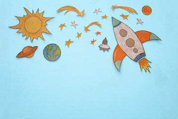 Rocket cut from paper and painted over wooden blue background.