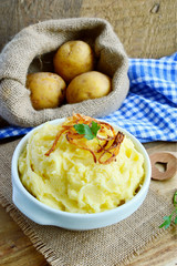 Mashed potatoes or Puree in white bowl with Crisp onion and parsley on wooden background.
