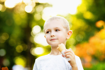 Happy little boy is eating ice cream outdoors at festive summer park background.