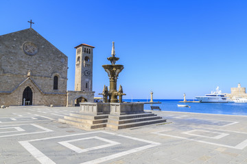 Fountain in Madraki port with Evangelismos chuch and clock tower in Rhodes, Dodecanese, Greece