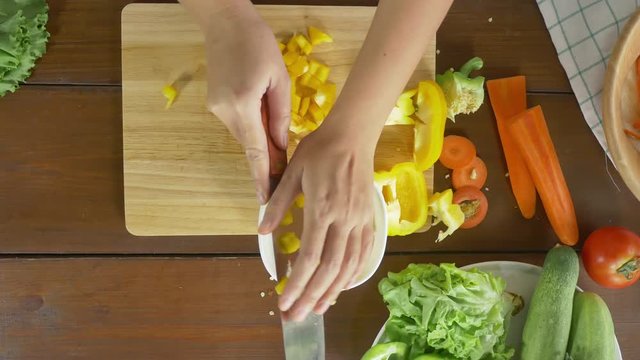 Top view of woman chief making salad healthy food and chopping bell pepper on cutting board in the kitchen.