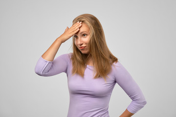 Cheerful pretty young European female making facepalm, holding hand on forehead, did something...