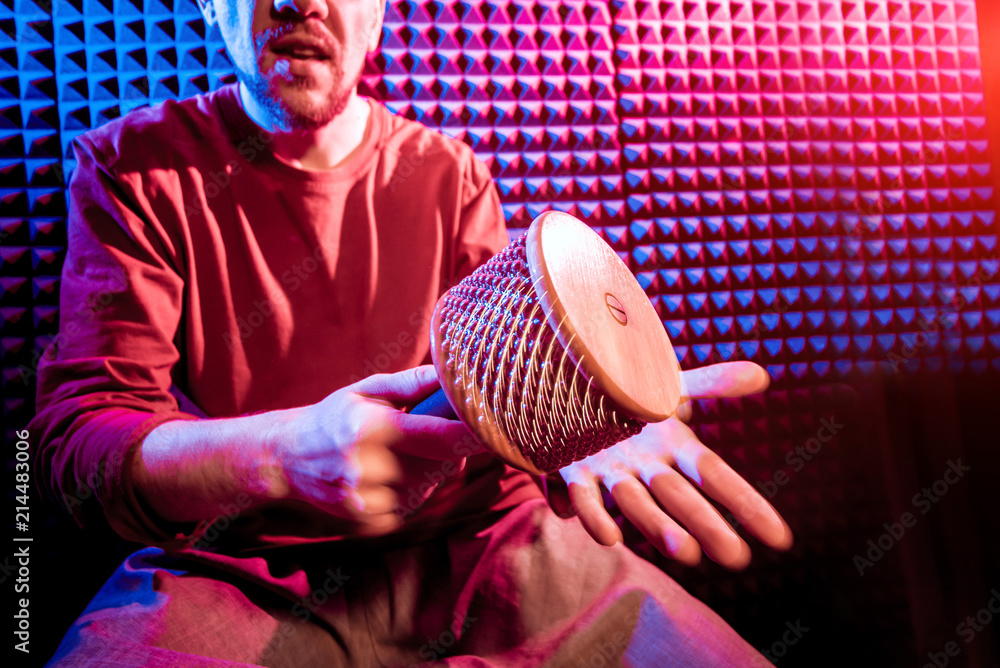 Wall mural Young man playing on maracas in sound recording studio.