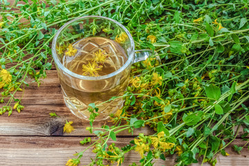 Cup of herbal tea from Hypericum - St. John's wort plant on wooden board table.