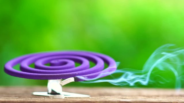 Slow Motion : Violet mosquito repellent and white smoke on wooden table with green blur light space background
