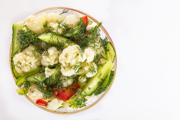 Fresh salad of cauliflower with cucumber, broccoli and greens, olives and sweet pepper in a glass bowl on a white background. Top view. Copy space