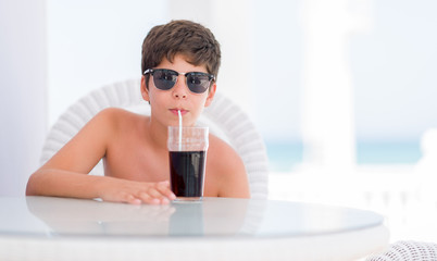 Young child on holidays drinking soda with a confident expression on smart face thinking serious