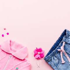 Little girl clothes collection flat lay with pink cardigan, jeans, sandals on pink background.