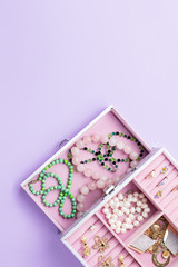 Open jewelry box with neclaces, earrings and rings on pastel background. Top view
