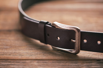 Leather belt on a wooden table - obrazy, fototapety, plakaty