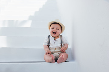 Beautiful baby sitting on white stairs in Santorini, Greece, wearing a hat and a vintage outfit