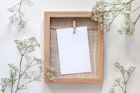 A wooden frame with a white mockup card and white flowers all around