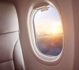 Airplane interior with window view of sunset above clouds.