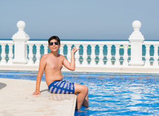 Young child on holiday at the swimming pool by the beach very happy pointing with hand and finger...