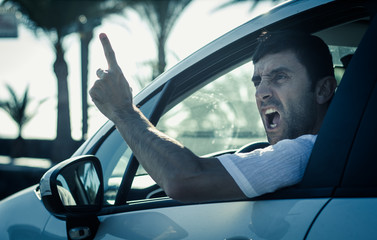 Furious man gesticulates with hand out of window while driving. Crazy driver yelling from car at...
