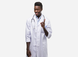 Young african american man wearing doctor coat surprised with an idea or question pointing finger...