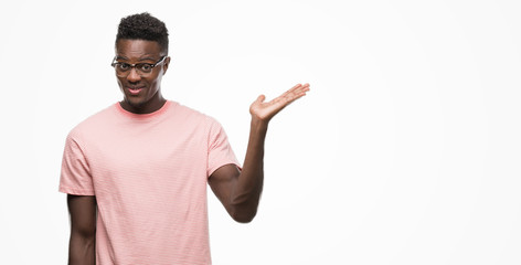 Young african american man wearing pink t-shirt smiling cheerful presenting and pointing with palm of hand looking at the camera.