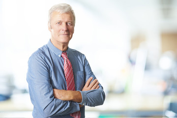 Executive senior manager portrait. A senior businessman standing at the office while looking at camera and smiling. 