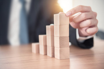 Close up Businessman hand arranging wood cube stacking as step stair. Business concept growth...