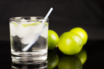 Alcohol drink (Gin Tonic cocktail) with lime and ice on black background with reflections